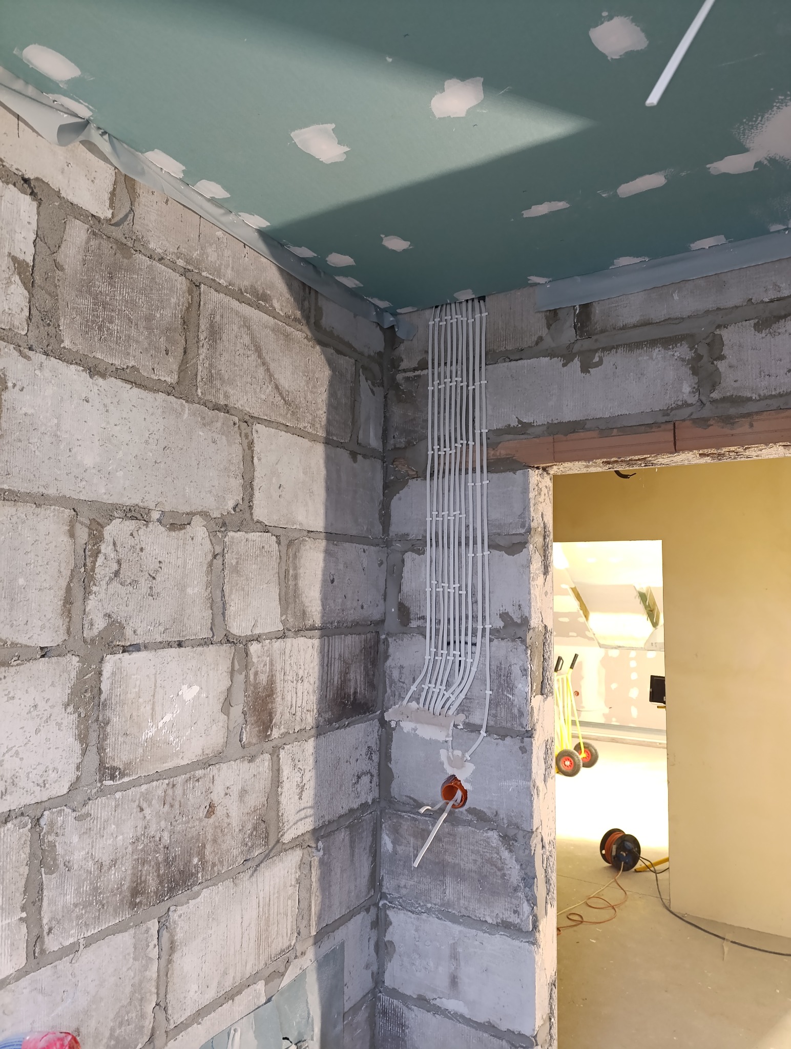Wewnętrzne okablowanie elektryczne prowadzone po ścianie z bloczków betonowych, zabezpieczone listwami, w surowym stanie, widoczne narzędzia w tle.
