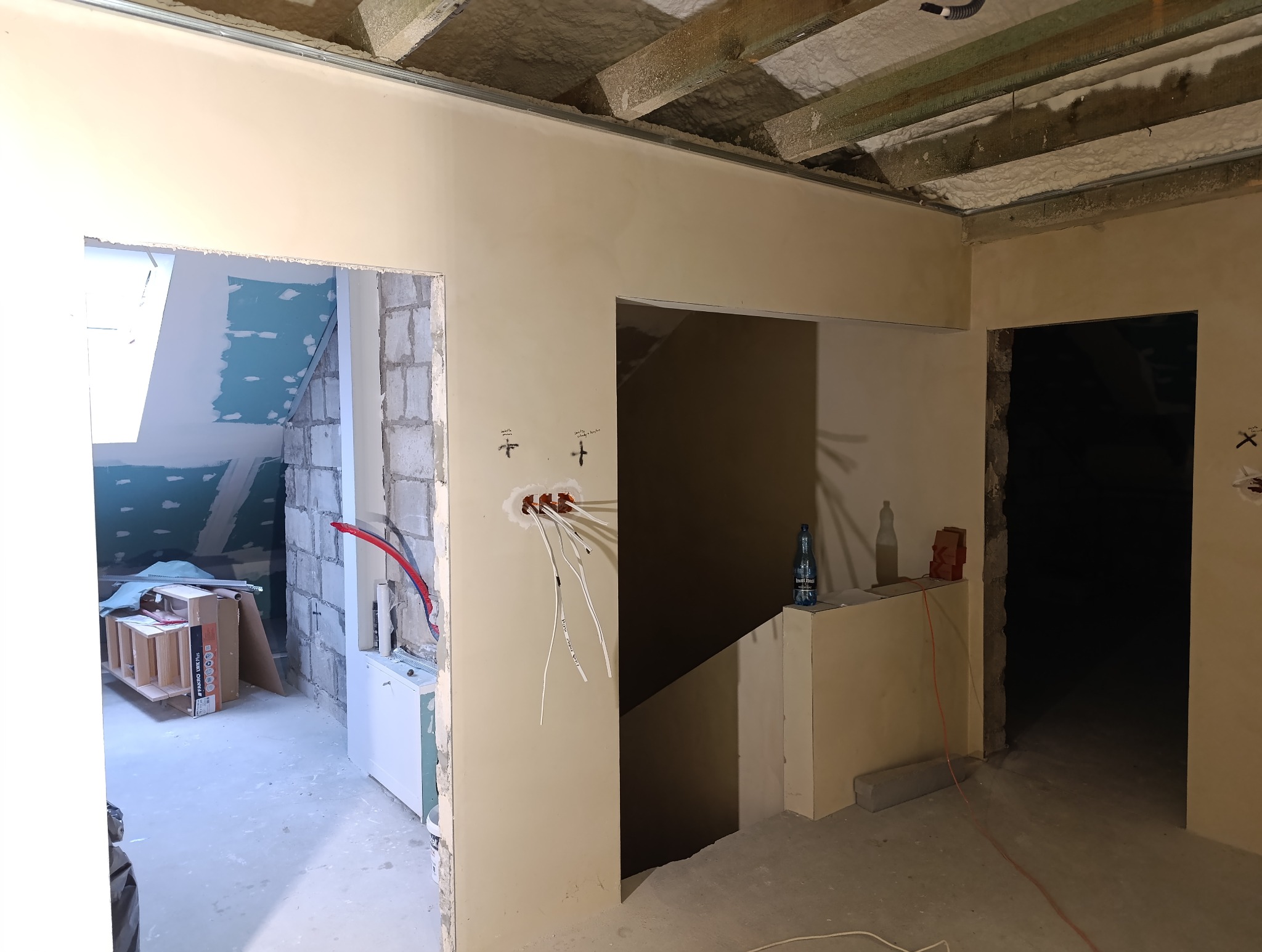 Wnętrze w trakcie remontu w Biłgoraju: widoczne przewody elektryczne wystające ze ściany, surowy strop z izolacją, ściany w trakcie szpachlowania, otwory drzwiowe w stanie deweloperskim.