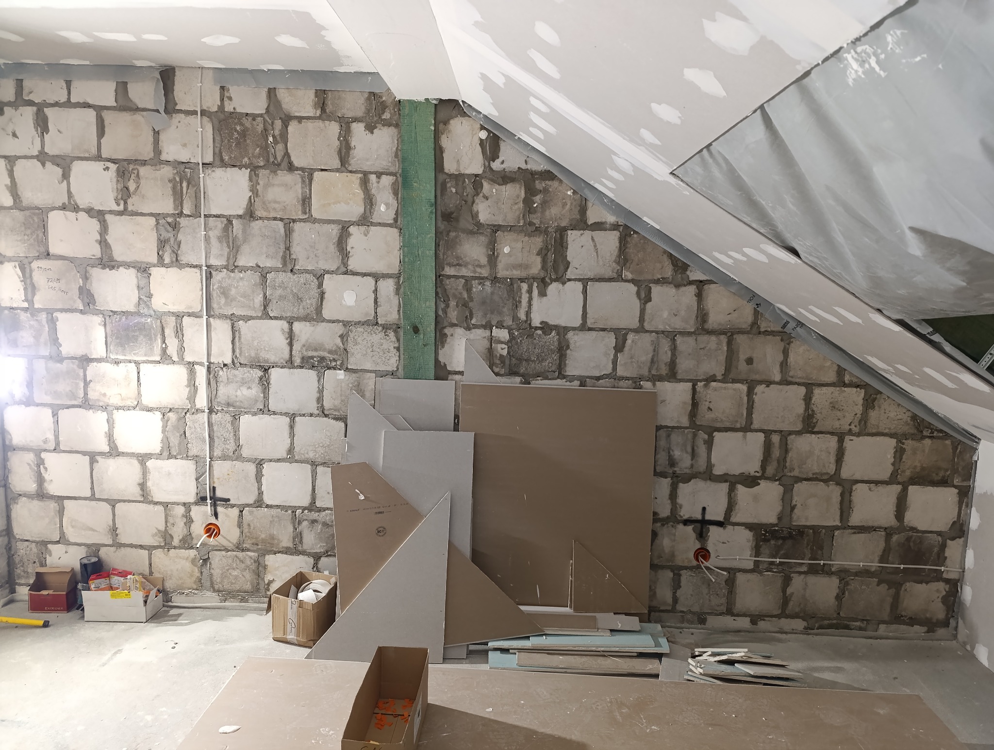 Surowa ściana z pustaków z widoczną instalacją elektryczną w trakcie montażu, częściowo zakryta płytami kartonowo-gipsowymi w pomieszczeniu na poddaszu.