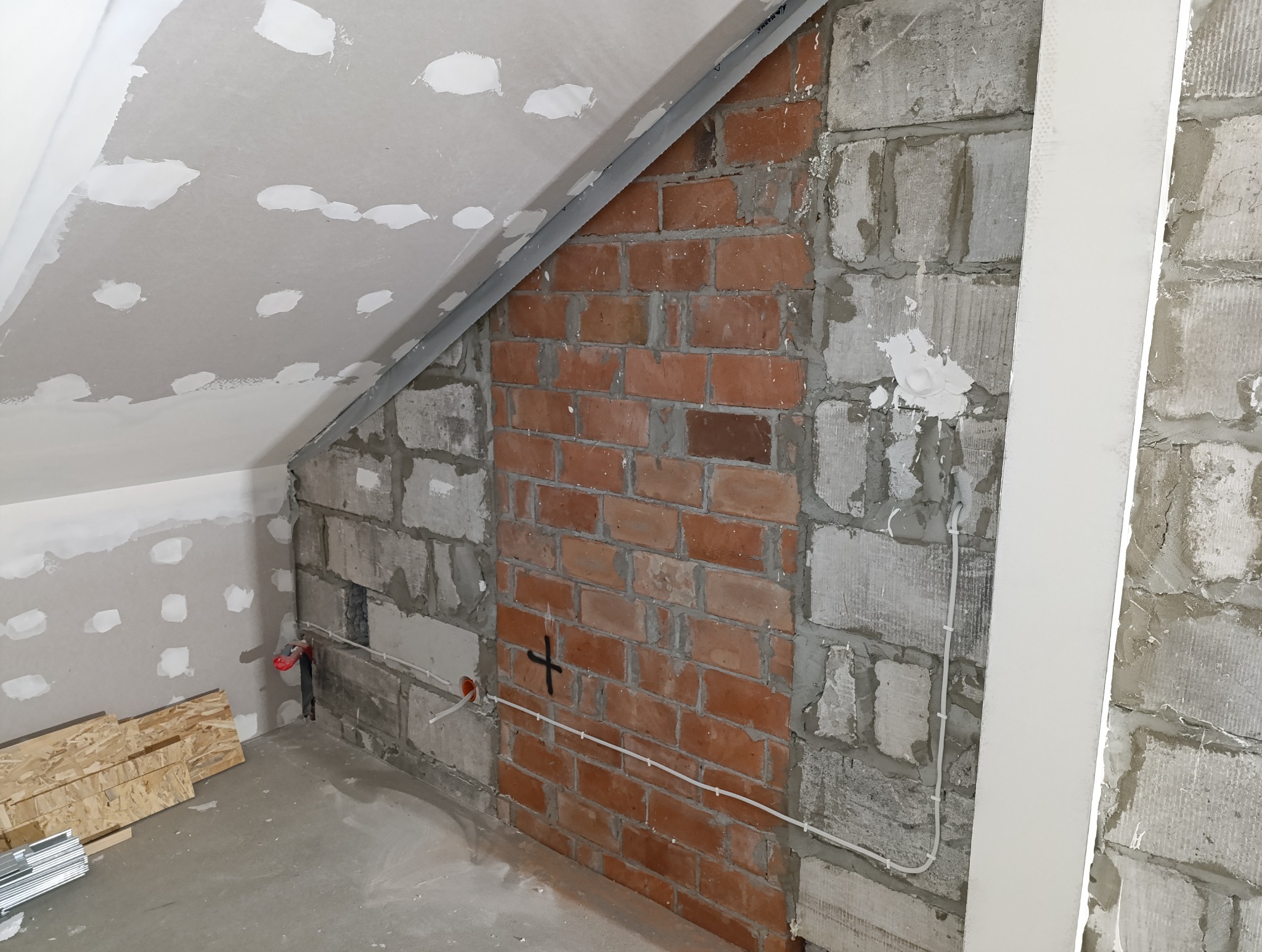 Adaptacja poddasza: ściana z cegły klinkierowej obudowana bloczkami betonowymi, instalacja elektryczna w peszlu, sufit z płyt gipsowo-kartonowych w trakcie szpachlowania, widoczne kable i puszki...