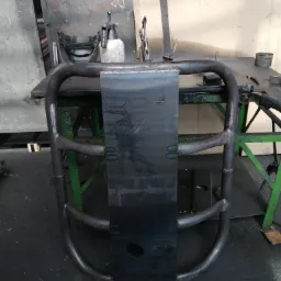 Surowa, spawana konstrukcja z rur stalowych i blachy na warsztatowym stole, widoczne ślady spawania i narzędzia.