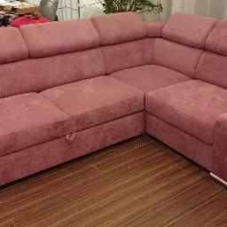 Różowa, narożna sofa z regulowanymi zagłówkami i metalowymi nóżkami, ustawiona na drewnianej podłodze.