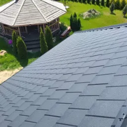 Nowy dach pokryty szarym gontem bitumicznym Novatik, widok z góry na tle altany i zielonego ogrodu.