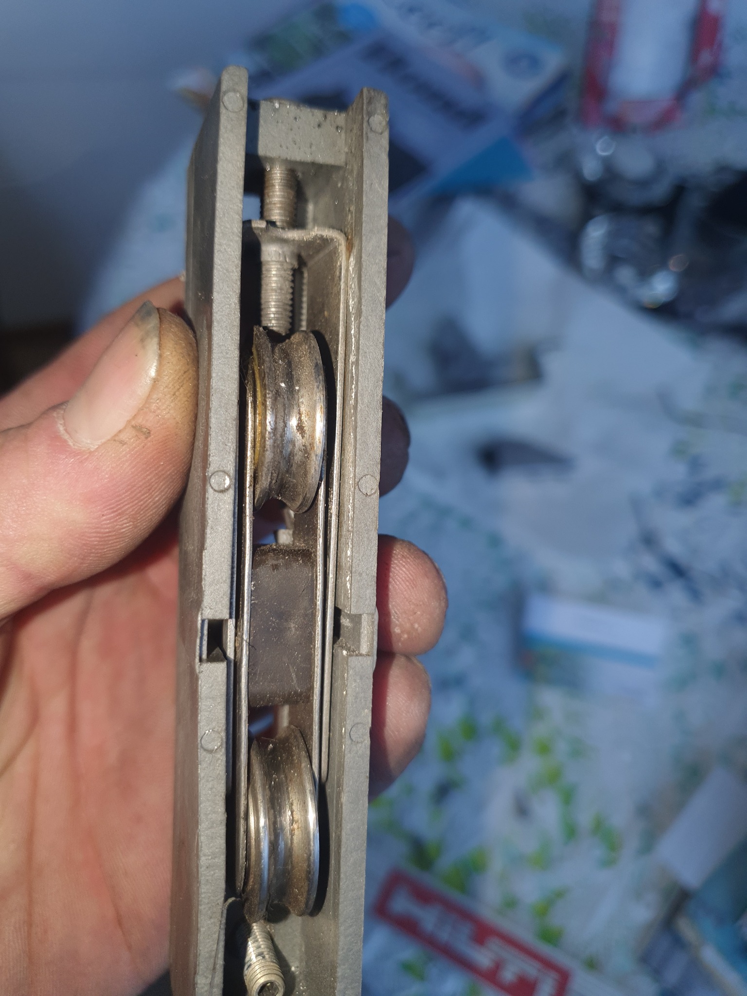 Detail of a dirty window sash balance with visible rollers and springs, held by a hand with visible dirt on the fingers, suggesting maintenance or repair work.