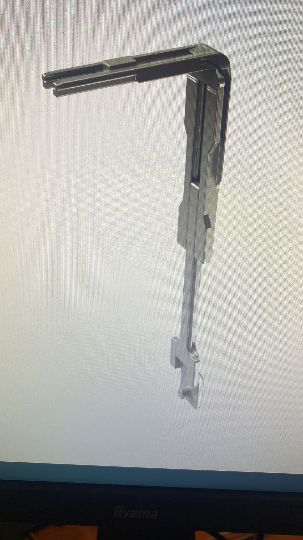 Metalowy kątownik okienny z elementami mocującymi, widoczny na tle ekranu monitora.