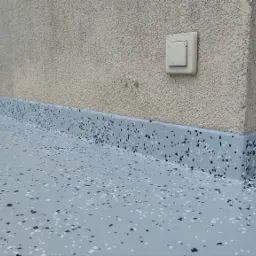 Szara, żywiczna posadzka z czarnymi i białymi elementami dekoracyjnymi, wykończona przy ścianie, z widocznym gniazdkiem i zabezpieczeniem folią malarską.