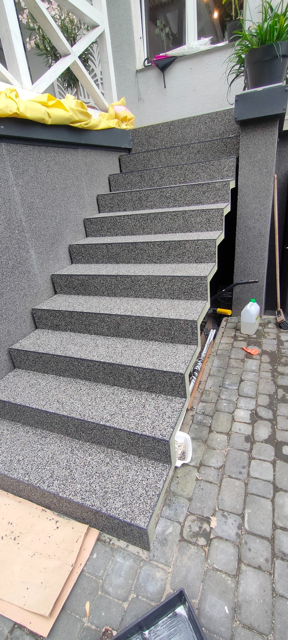 Schody zewnętrzne wykończone szarą, kamyczkową mozaiką żywiczną, widoczne narzędzia i materiały budowlane. Nowoczesny design, solidne wykonanie.
