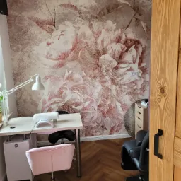 Salon kosmetyczny z fototapetą w kwiaty, biurkiem, lampą, krzesłem i sprzętem do manicure.