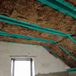 Poddasze w trakcie ocieplania: wełna mineralna między zielonymi profilami, widoczny fragment okna i surowych ścian z betonu komórkowego.