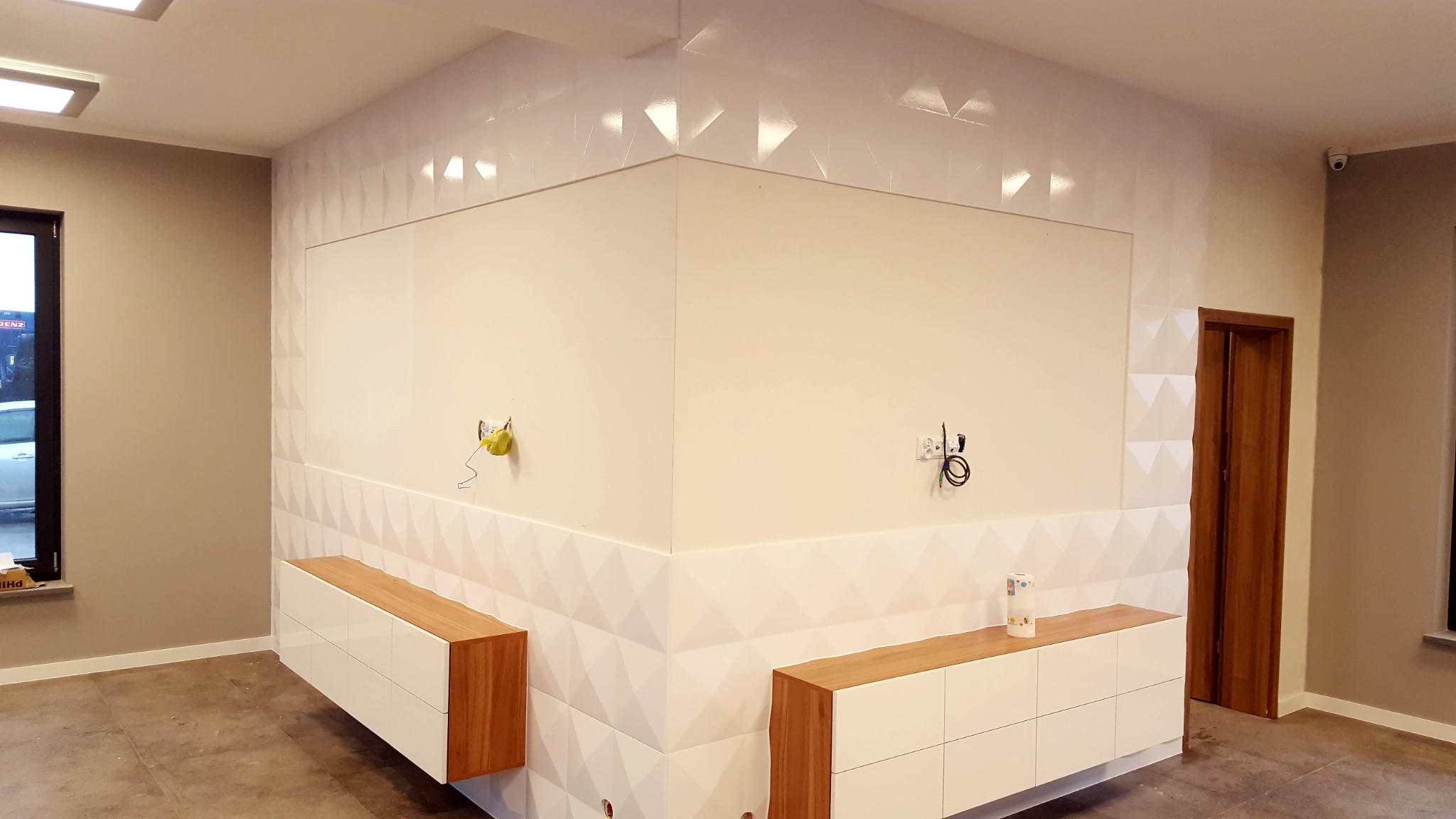 Nowoczesne wnętrze w Mirachowie z białymi płytkami o geometrycznym wzorze 3D na ścianach, szafki z drewnianym blatem, widoczne przygotowane punkty elektryczne.