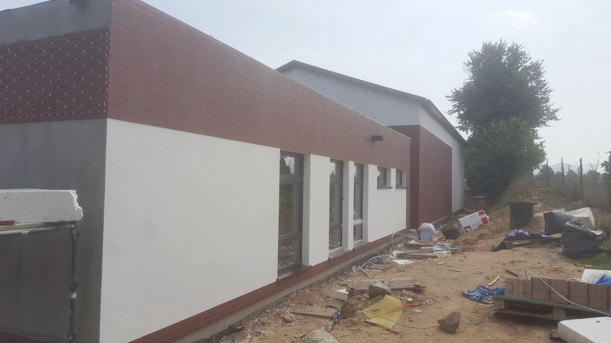 Elewacja budynku z częściowo wykończoną klinkierową okładziną, widoczne fragmenty ocieplenia i niezakończone prace wykończeniowe na zewnątrz.