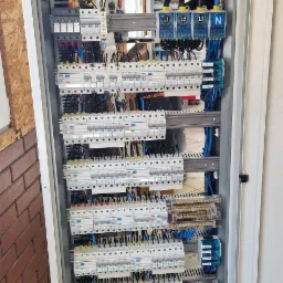 Otwarta szafa elektryczna z licznymi bezpiecznikami, listwami zaciskowymi i okablowaniem, widok z góry na dół, ukazujący złożoność i porządek instalacji.