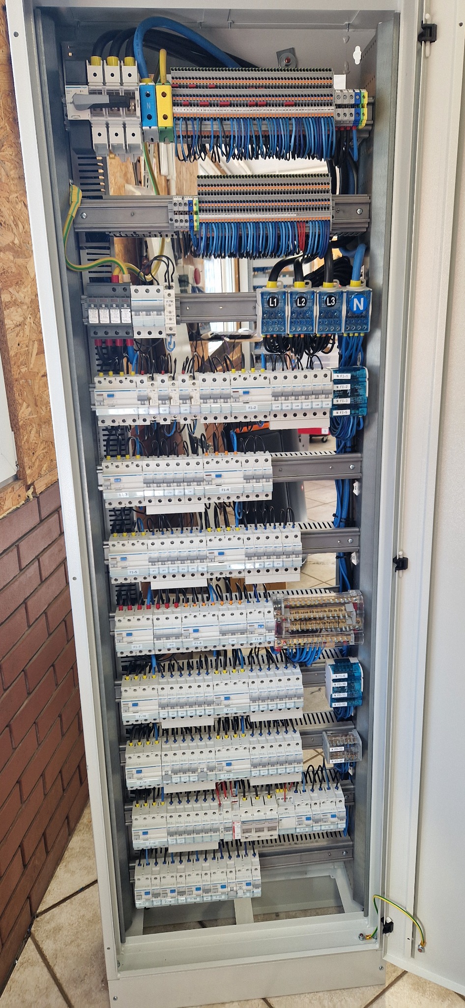 Otwarta szafa elektryczna z licznymi bezpiecznikami, listwami zaciskowymi i okablowaniem, widok z góry na dół, ukazujący złożoność i porządek instalacji.