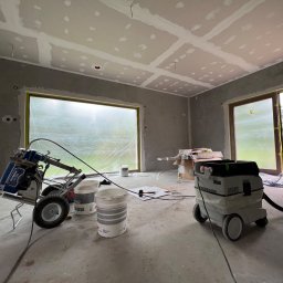 GRUBE WAŁKI SPÓŁKA Z OGRANICZONĄ ODPOWIEDZIALNOŚCIĄ - Wnętrze w trakcie prac wykończeniowych: ściany przygotowane pod malowanie, sufit z płyt kartonowo-gipsowych, sprzęt malarski i odkurzacz przemysłowy. Okna zabezpieczone folią.