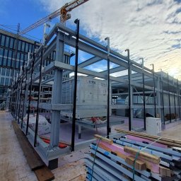 WB-Fassaden - Wznoszenie stalowej konstrukcji hali w Jabłonnie, widoczne elementy wentylacji, dźwig w tle i pracownik w odblaskowej kamizelce.