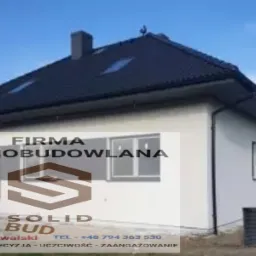 Dom jednorodzinny z ciemną dachówką i białą elewacją, widoczny z boku, z logo firmy budowlanej nałożonym na zdjęcie.