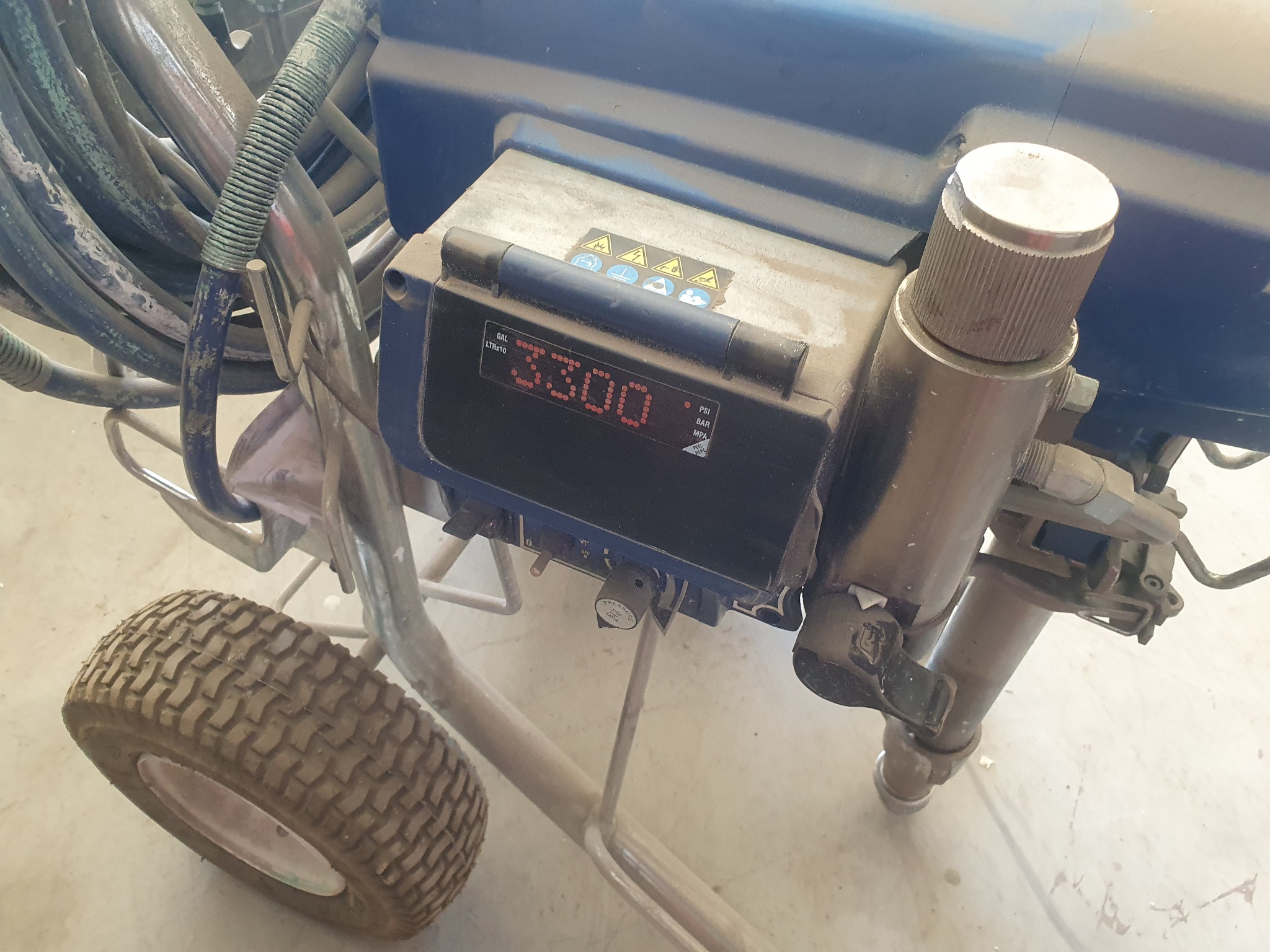 Zbliżenie na brudny, niebieski agregat malarski na kółkach z wyświetlaczem wskazującym 3300 jednostek, z widocznymi przewodami i elementami regulacyjnymi.