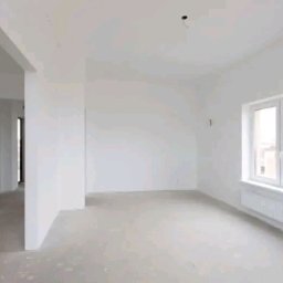 Pawlowolochastyi - Pusty, jasny pokój po szpachlowaniu, z widoczną gładzią na ścianach, przygotowany do dalszych prac wykończeniowych, z oknem i grzejnikiem.