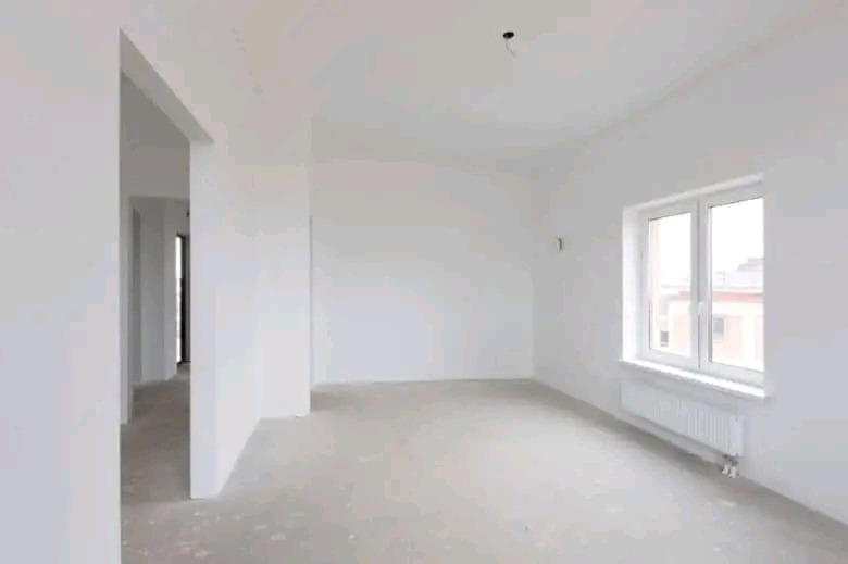 Pusty, jasny pokój po szpachlowaniu, z widoczną gładzią na ścianach, przygotowany do dalszych prac wykończeniowych, z oknem i grzejnikiem.