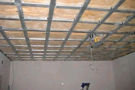 Metalowa konstrukcja sufitu podwieszanego z wypełnieniem płytami OSB, widoczna drabina i narzędzia elektryczne.