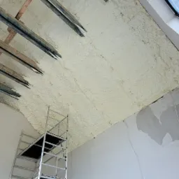 Poddasze w trakcie ocieplania pianką PUR, widoczne drewniane elementy konstrukcyjne, rusztowanie i fragment okna dachowego.