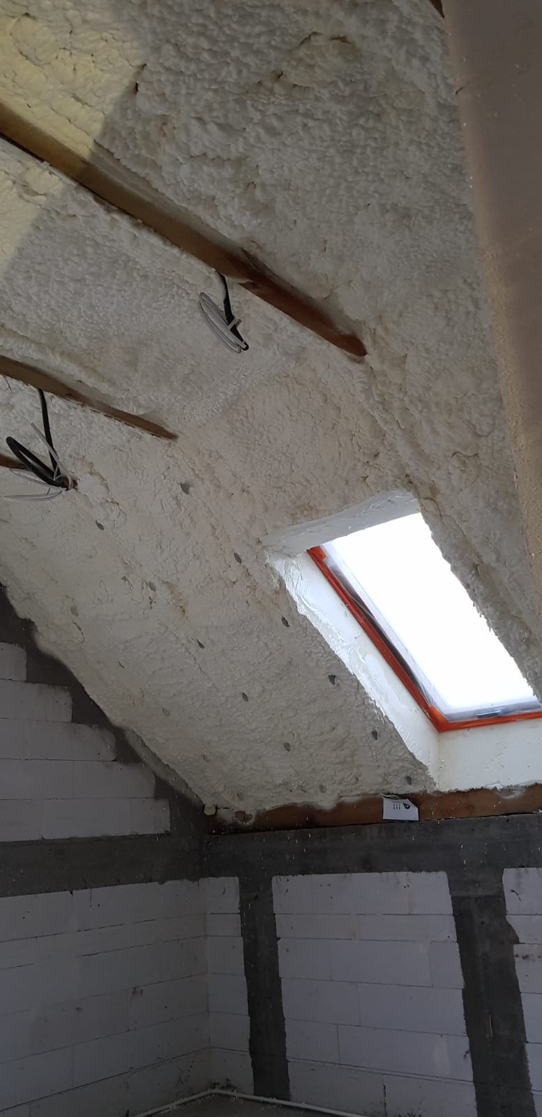 Poddasze z oknem dachowym po ociepleniu pianką, widoczne krokwie i ściany z betonu komórkowego.