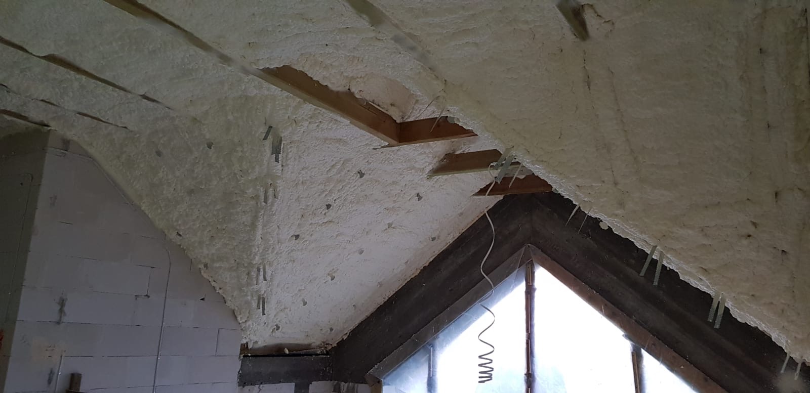 Poddasze ocieplone pianką PUR, widoczne drewniane elementy konstrukcyjne i okno dachowe, z pozostałościami pianki na framugach.