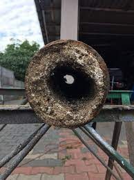 Przekrój rury kanalizacyjnej silnie zanieczyszczonej osadami, widoczny mały otwór przepływowy.