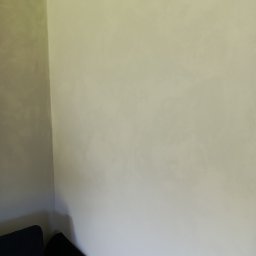 Michał  Wojtas - Ściana po szpachlowaniu z efektem dekoracyjnym, widoczna z narożnika pokoju, z fragmentem ciemnej sofy i poduszki w kwiaty.