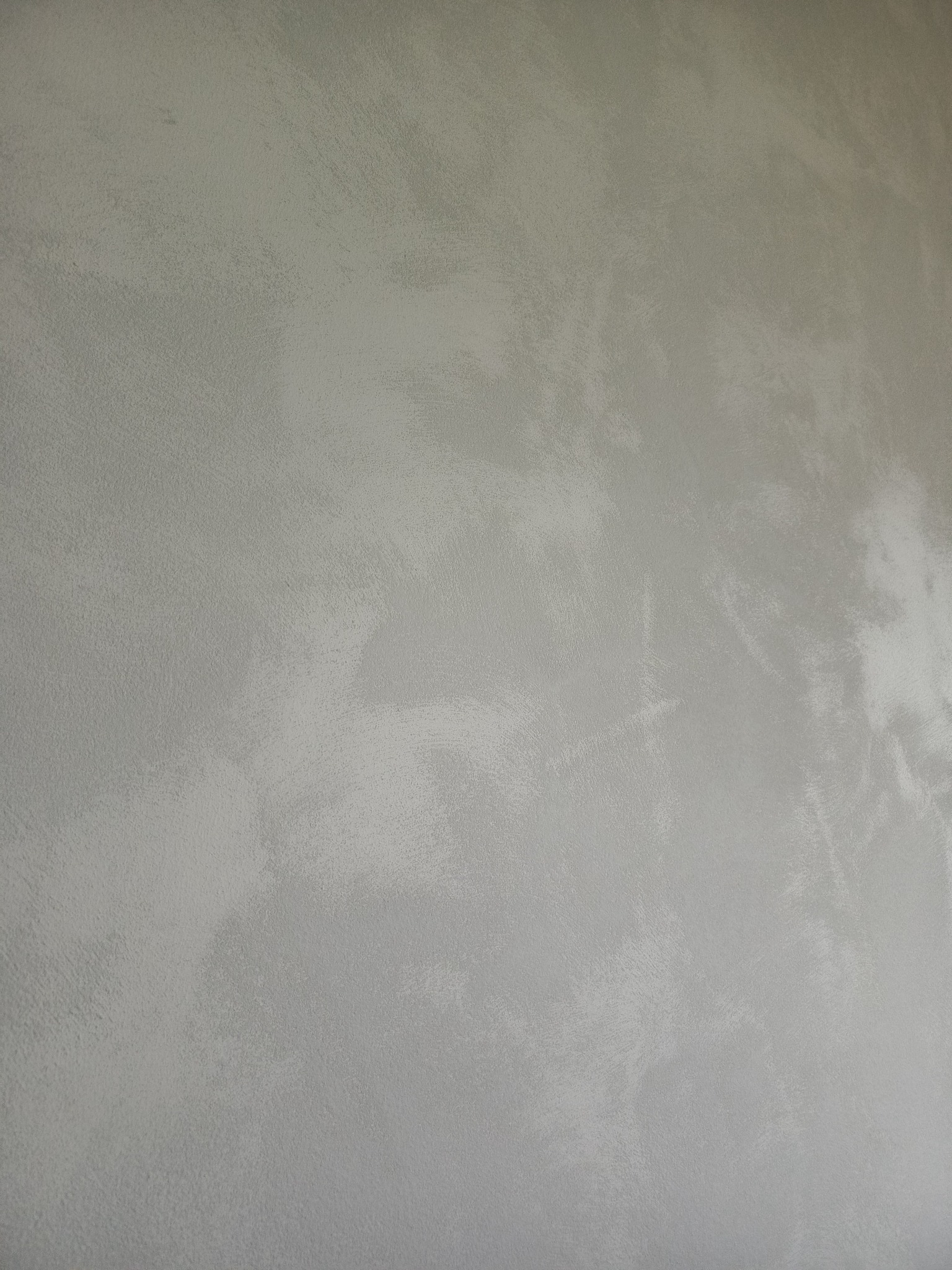 Jasnoszara ściana z efektem dekoracyjnym, imitującym przecierkę, gładka powierzchnia z subtelnymi zmianami odcieni. Minimalistyczny design, brak detali.