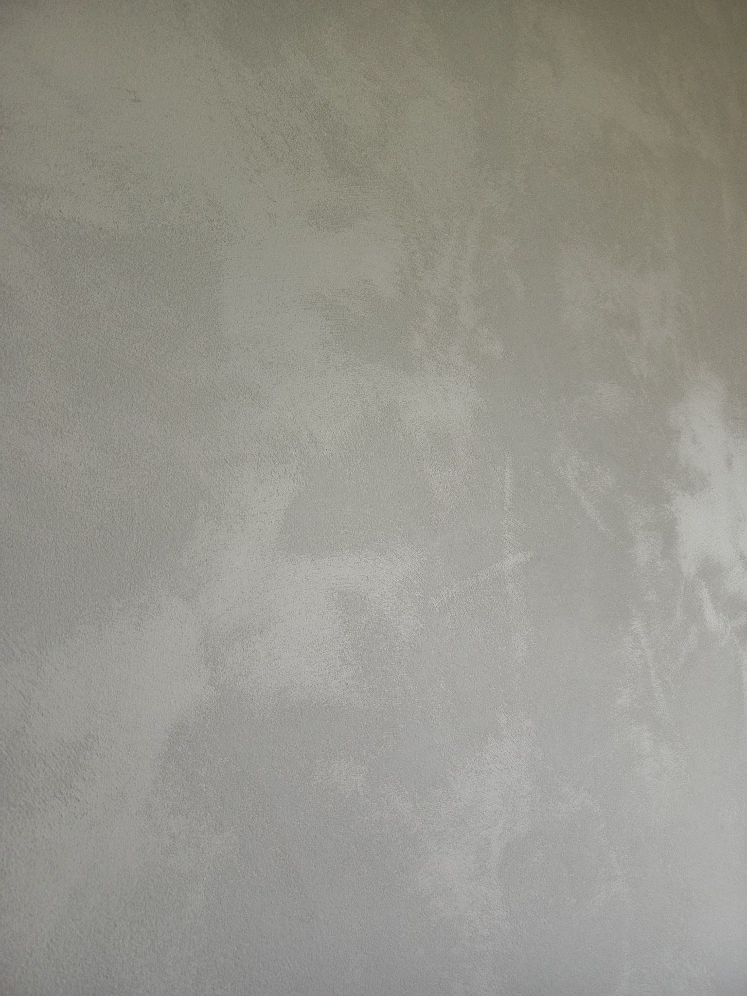 Szara, gładka ściana z efektem delikatnego cieniowania, wykonana techniką dekoracyjną. Widoczna struktura i subtelne przejścia tonalne. Minimalistyczny design.