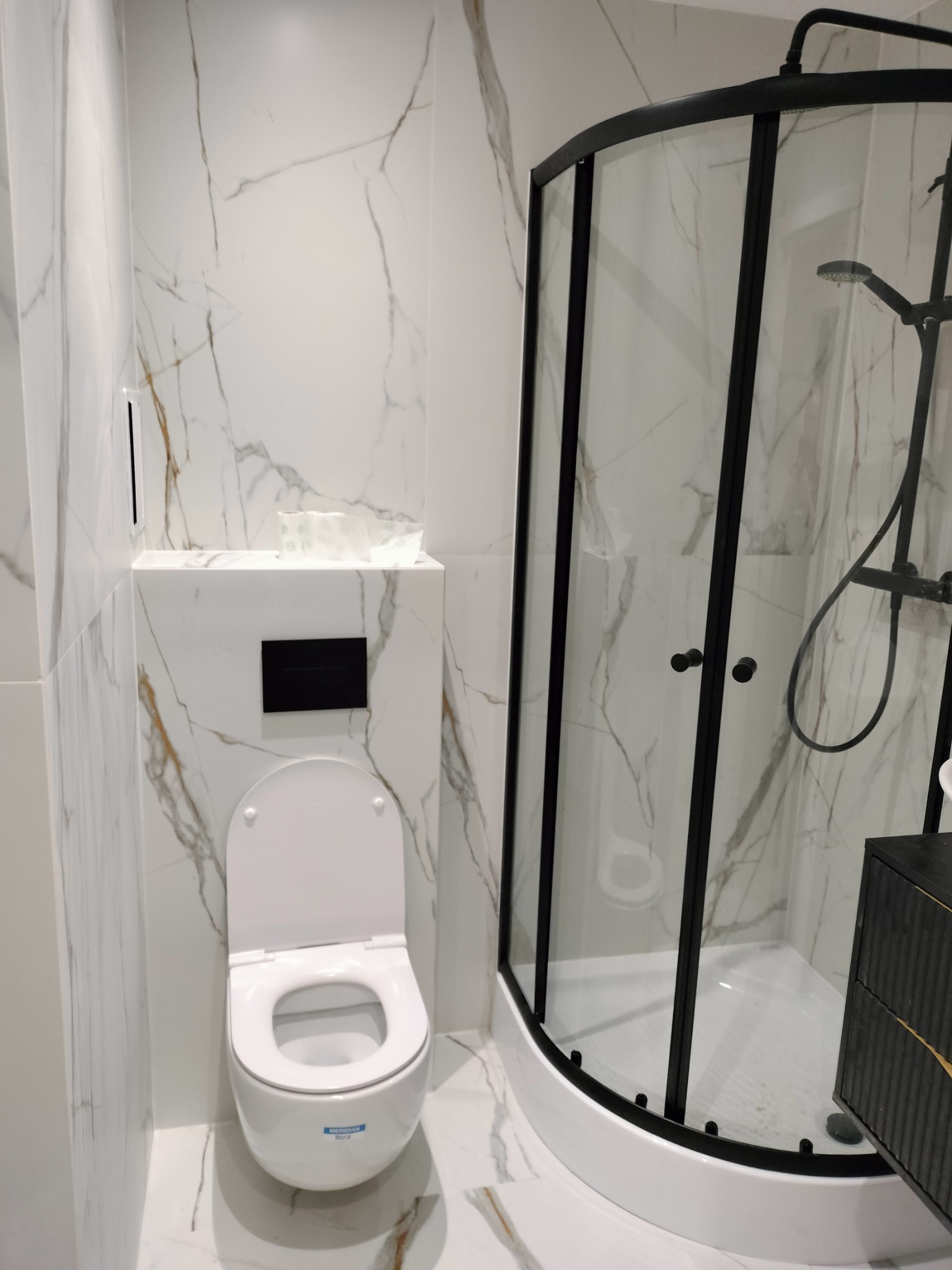 Nowoczesna łazienka z kabiną prysznicową w czarnej ramie i podwieszaną toaletą, wykończona marmurowymi płytkami z delikatnym złotym żyłowaniem.
