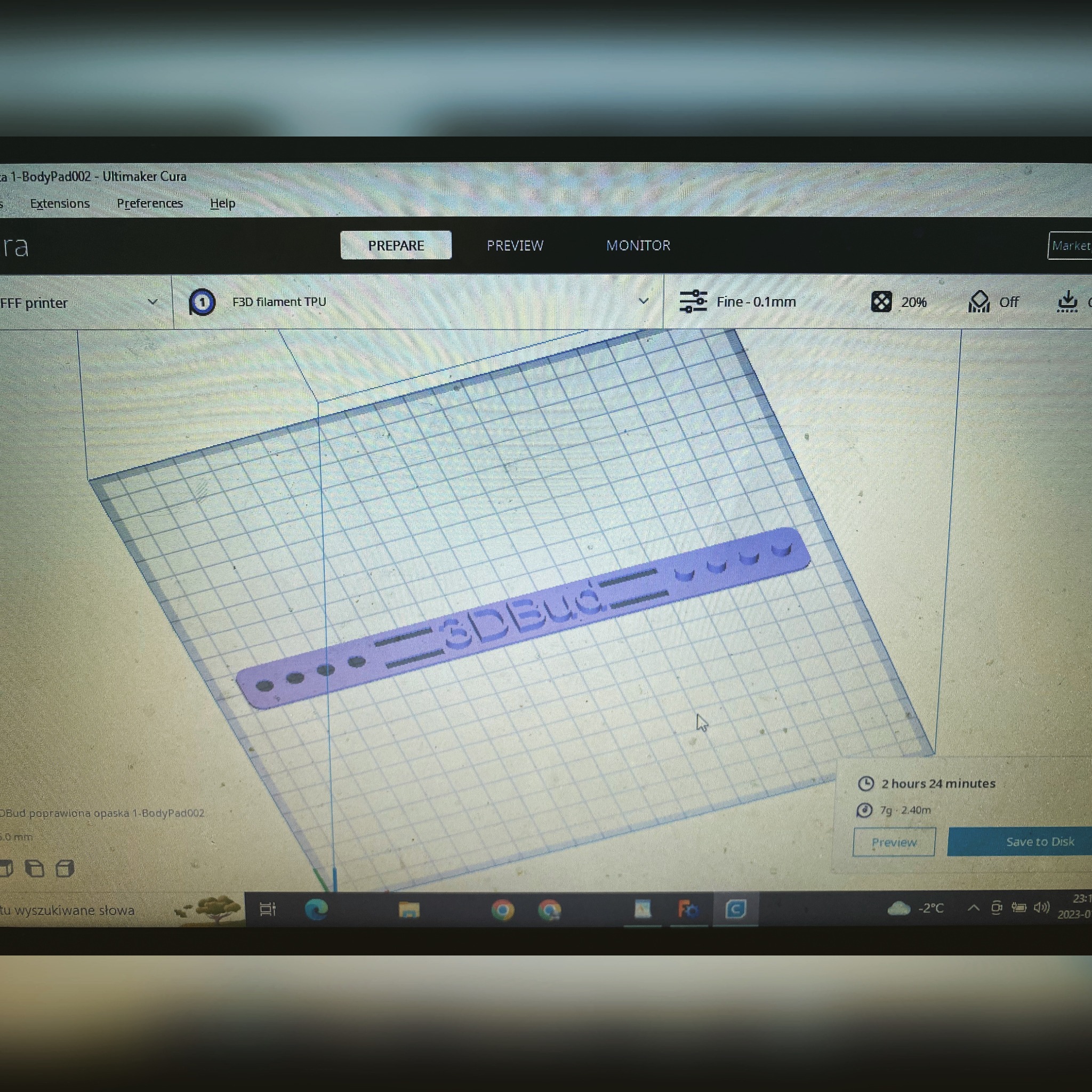 Widok z ekranu komputera przedstawiający interfejs programu Ultimaker Cura z modelem 3D opaski z napisem '3DBud' przygotowywanej do druku 3D, ustawienia druku widoczne na ekranie.