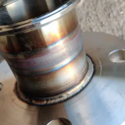 Spoina obwodowa rury ze stali nierdzewnej do kołnierza, widoczne przebarwienia termiczne i ślady szlifowania, trzymana w rękawicy roboczej.