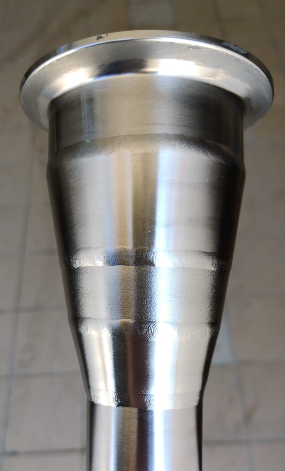 Metalowy element rurowy ze śladami spawania, widoczne okręgi po spawaniu TIG, lekko stożkowy kształt.