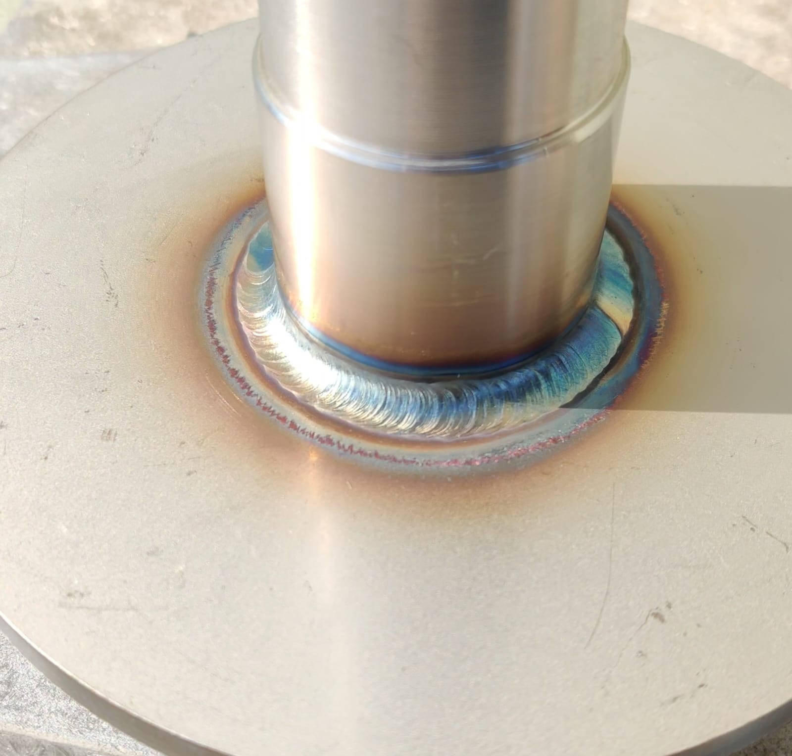 Precyzyjne spoiny TIG na okrągłej podstawie, widoczne charakterystyczne kolory hartowania metalu.