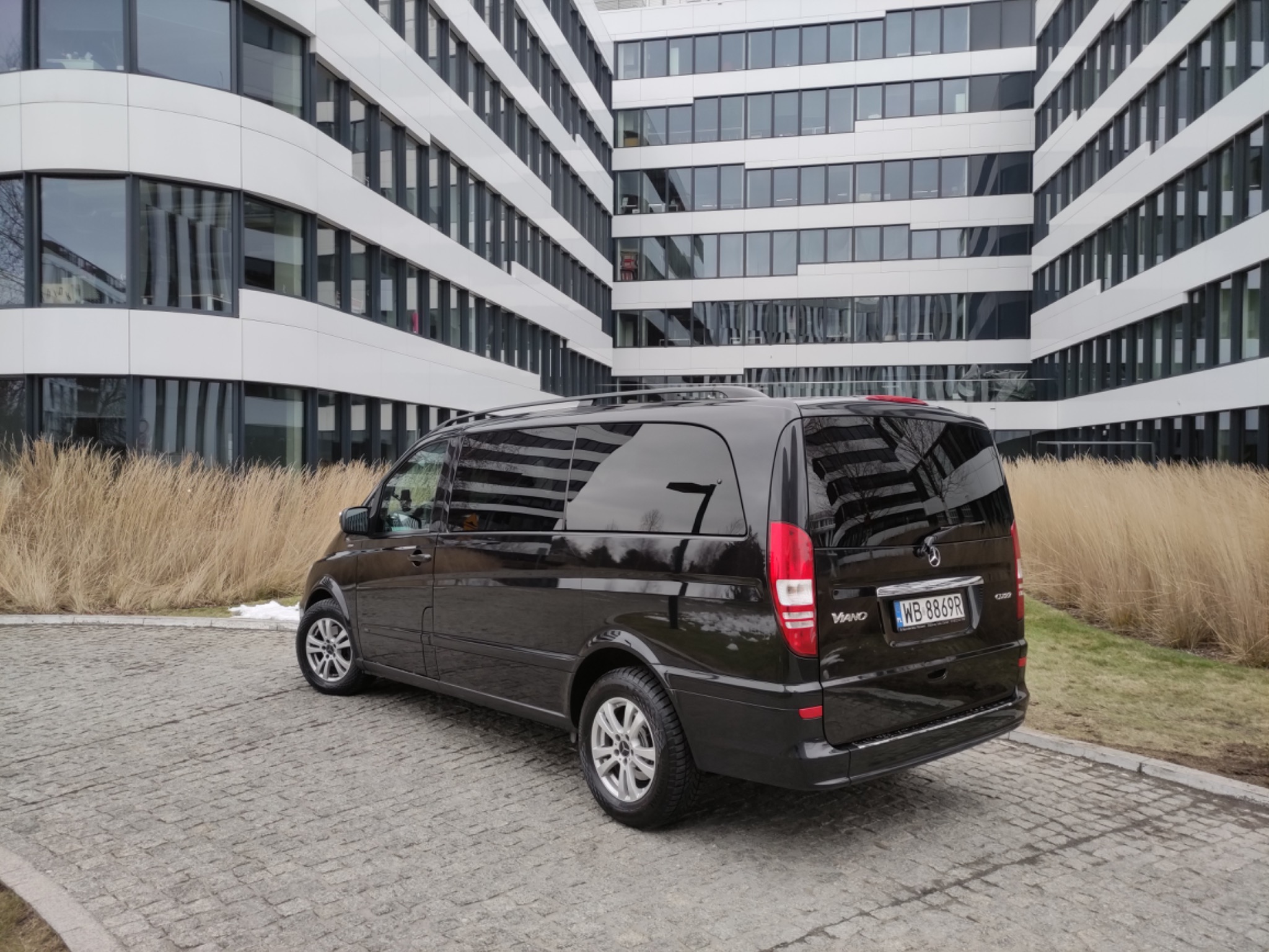 Czarny van Mercedes-Benz Viano zaparkowany przed nowoczesnym budynkiem biurowym z licznymi oknami, widoczny numer rejestracyjny WB 8869R.