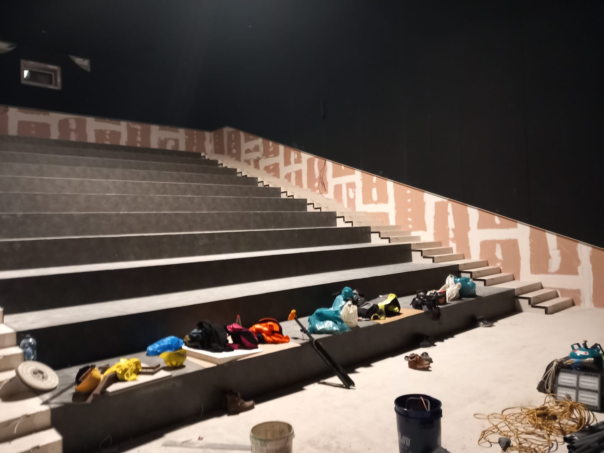 Szeroki kadr na schody w trakcie wykańczania, z widocznymi narzędziami i materiałami budowlanymi, na ścianie widoczne ślady po szpachlowaniu, ciemne tło sufitu, etap prac wykończeniowych.