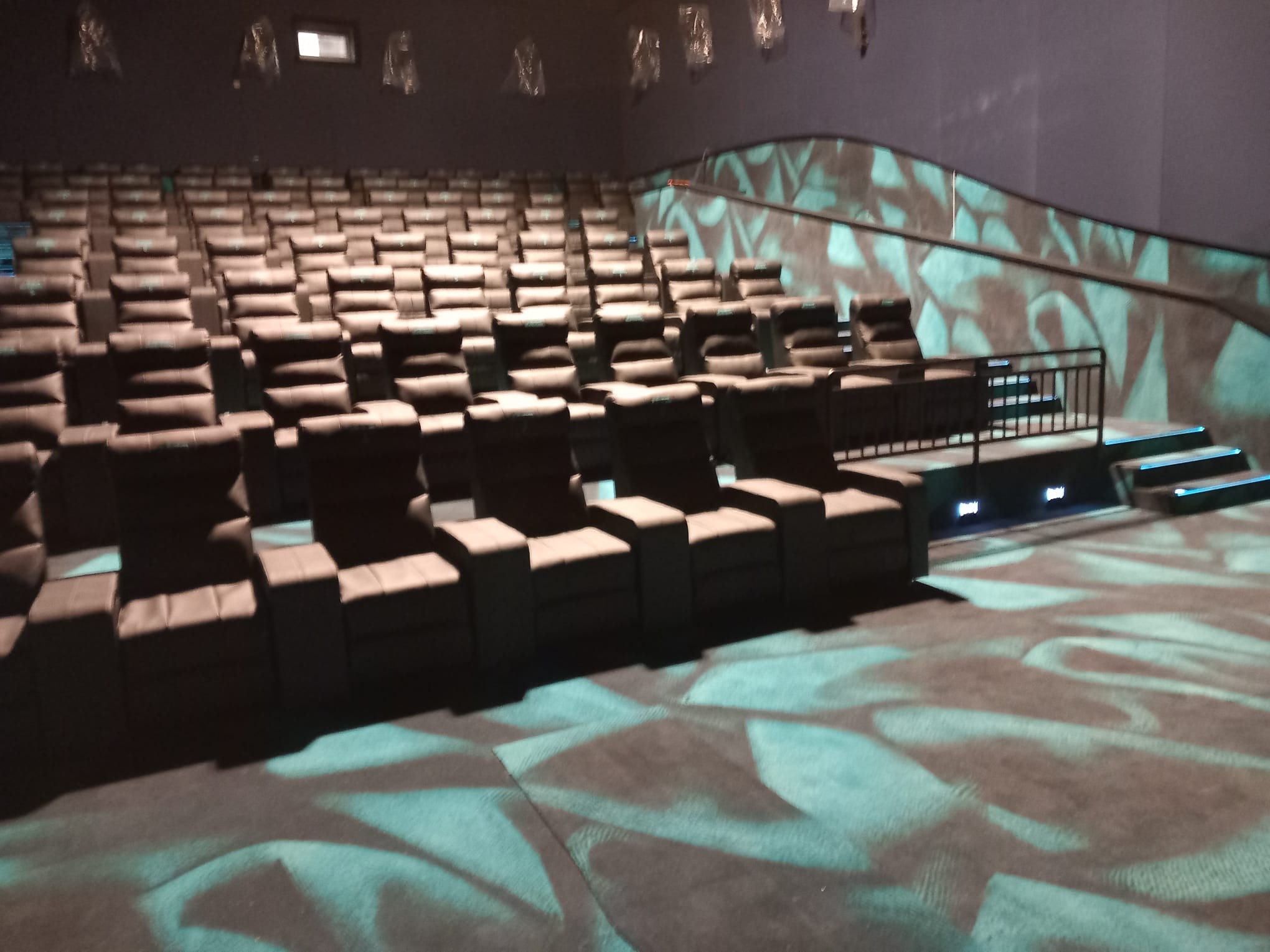 Rzędy ciemnoszarych, tapicerowanych foteli kinowych w nowym kinie, oświetlonych dekoracyjnym wzorem na podłodze i ścianach.