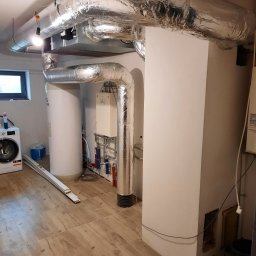 Opal-House - Kotłownia z piecem, zasobnikiem ciepłej wody i instalacją grzewczą z izolowanymi rurami, pralka w tle.