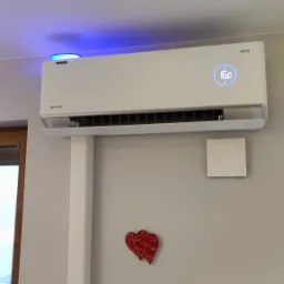 Biała klimatyzacja Rotenso FRESH z niebieską poświatą LED na ścianie, pod nią dekoracja w kształcie dwóch czerwonych serc.