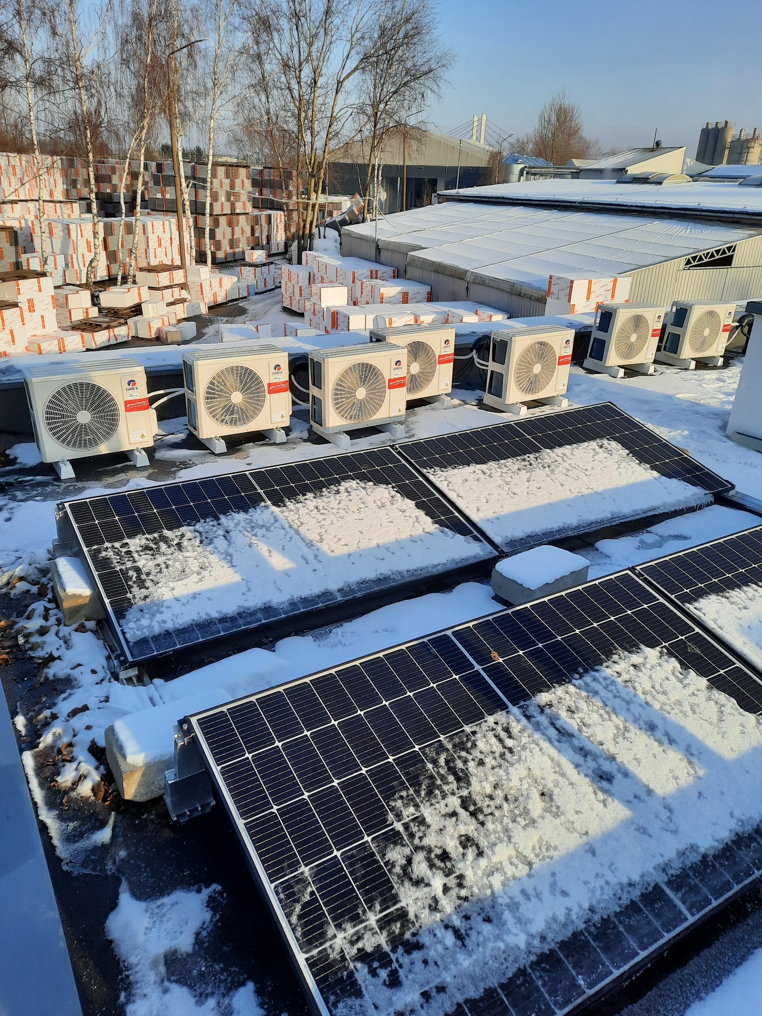 Instalacja paneli fotowoltaicznych i klimatyzacji na dachu w zimowej scenerii, częściowo pokryte śniegiem, z widocznymi jednostkami zewnętrznymi klimatyzatorów marki Gree.