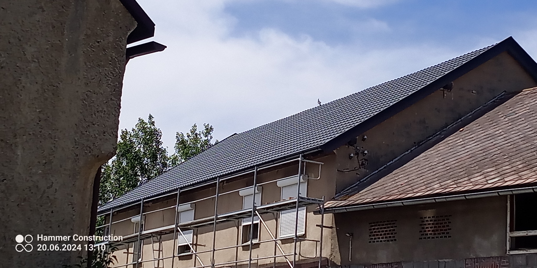 Dom w trakcie prac z nowym, ciemnoszarym pokryciem dachowym, widoczne rusztowanie, na dachu siedzi ptak.