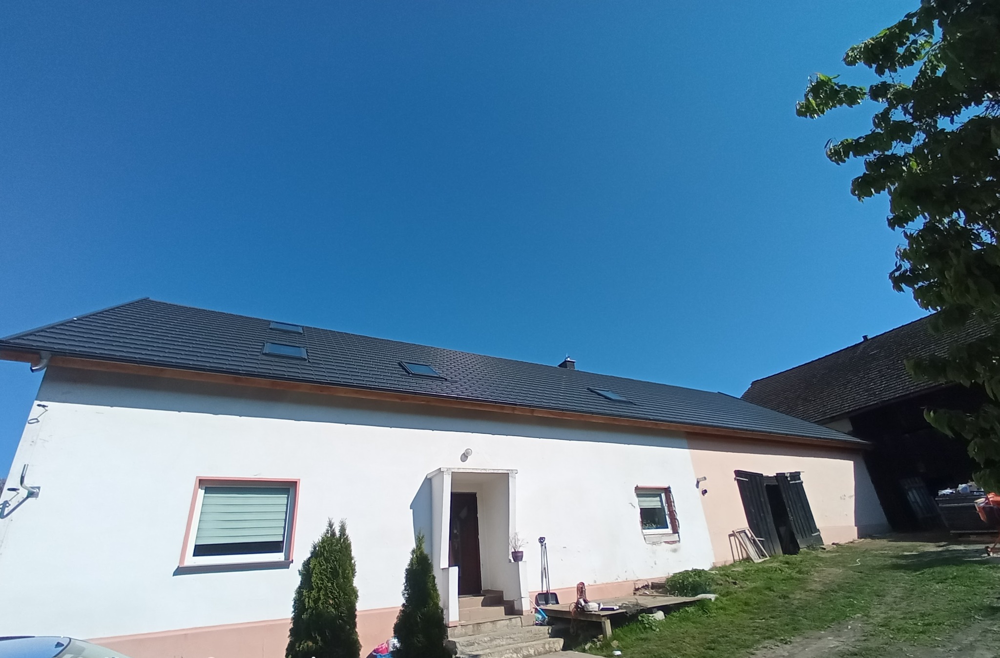 Dom jednorodzinny z nowym, grafitowym dachem z dachówką ceramiczną i oknami dachowymi, widok z poziomu gruntu w słoneczny dzień.