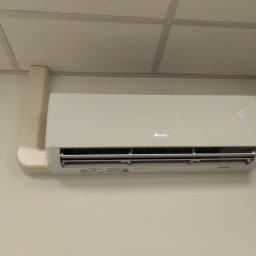 VibeKlim - Biała jednostka wewnętrzna klimatyzatora marki Gree zamontowana na jasnej ścianie, widoczny wyświetlacz z temperaturą 16 stopni Celsjusza i fragment instalacji odprowadzającej skropliny.