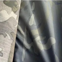 Fragmenty tkaniny w kamuflażu w odcieniach szarości i zieleni, widoczne fałdy i faktura materiału.