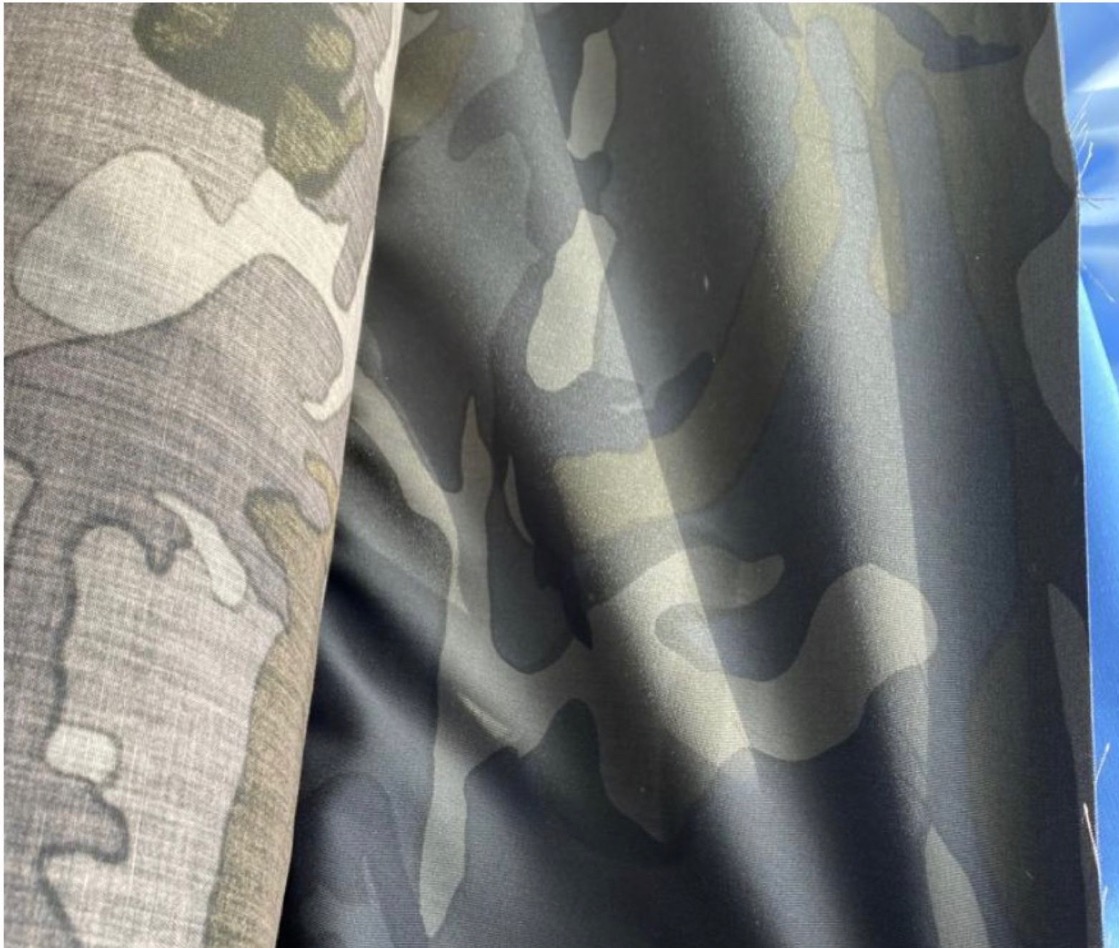 Fragmenty tkaniny w kamuflażu w odcieniach szarości i zieleni, widoczne fałdy i faktura materiału.