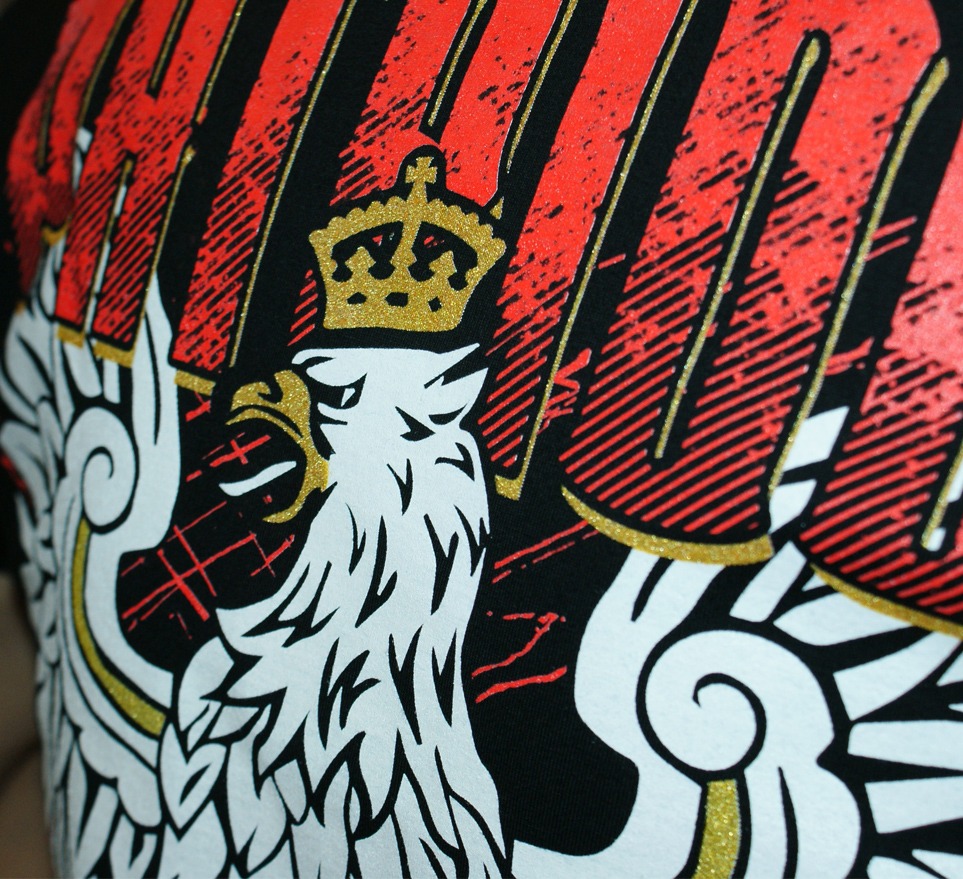 Czarny t-shirt z nadrukiem orła w koronie w barwach narodowych, zbliżenie na detal grafiki z efektem brokatu.