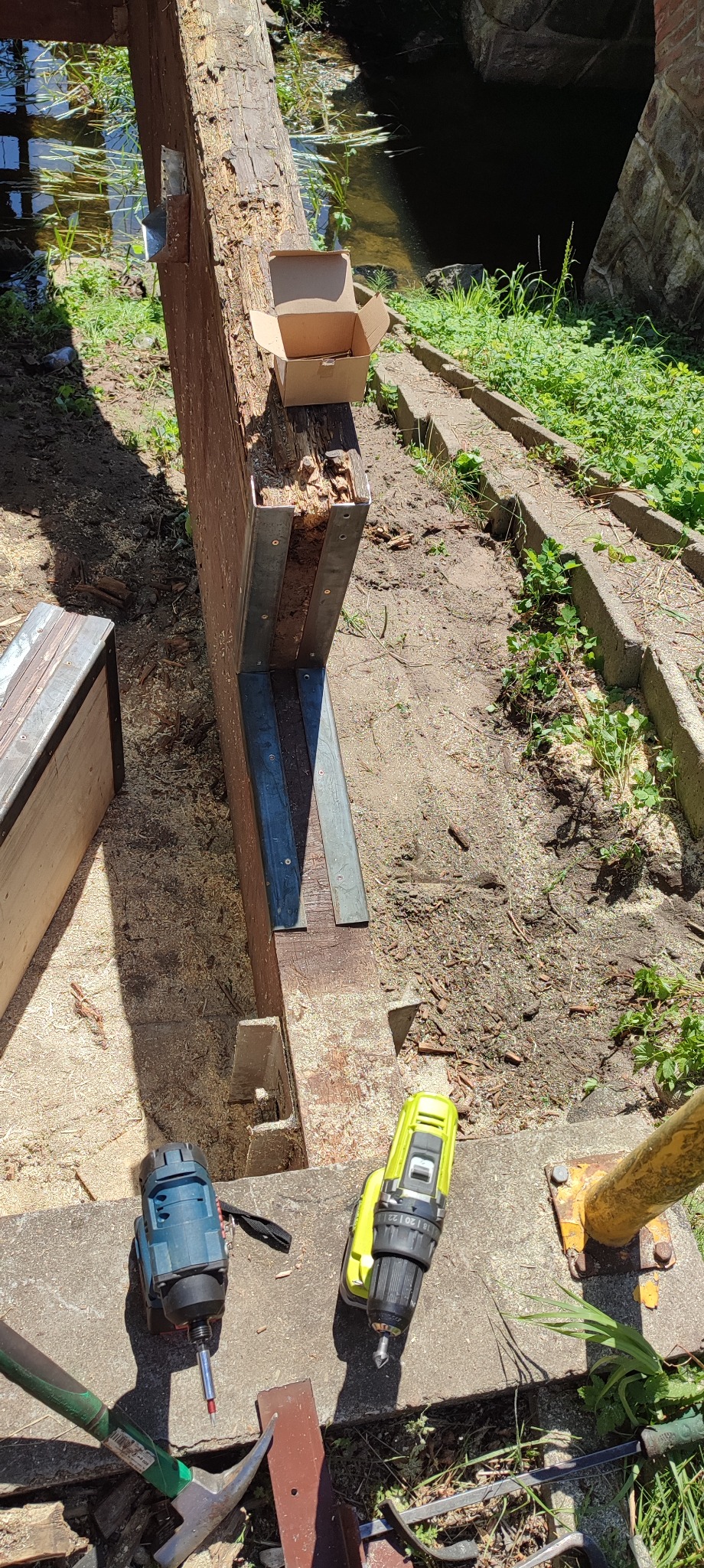 Drewniana konstrukcja wzmacniana metalowymi elementami, otoczona piaskiem i narzędziami, z widoczną rzeką w tle.