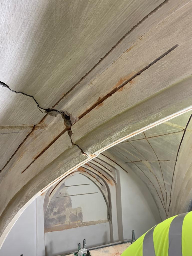 Pęknięte sklepienie łukowe z widocznymi elementami konstrukcyjnymi, ślady korozji i częściowo odspojony tynk, ujęcie z dołu podczas prac remontowych.